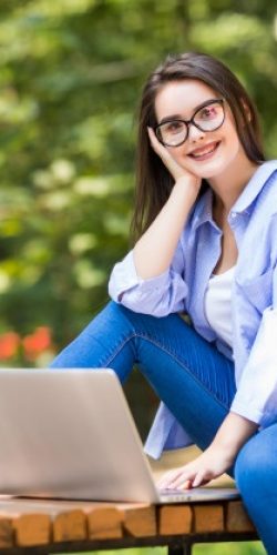 happy-female-student-sitting-bench-with-laptop-outdoors-campus_231208-4265